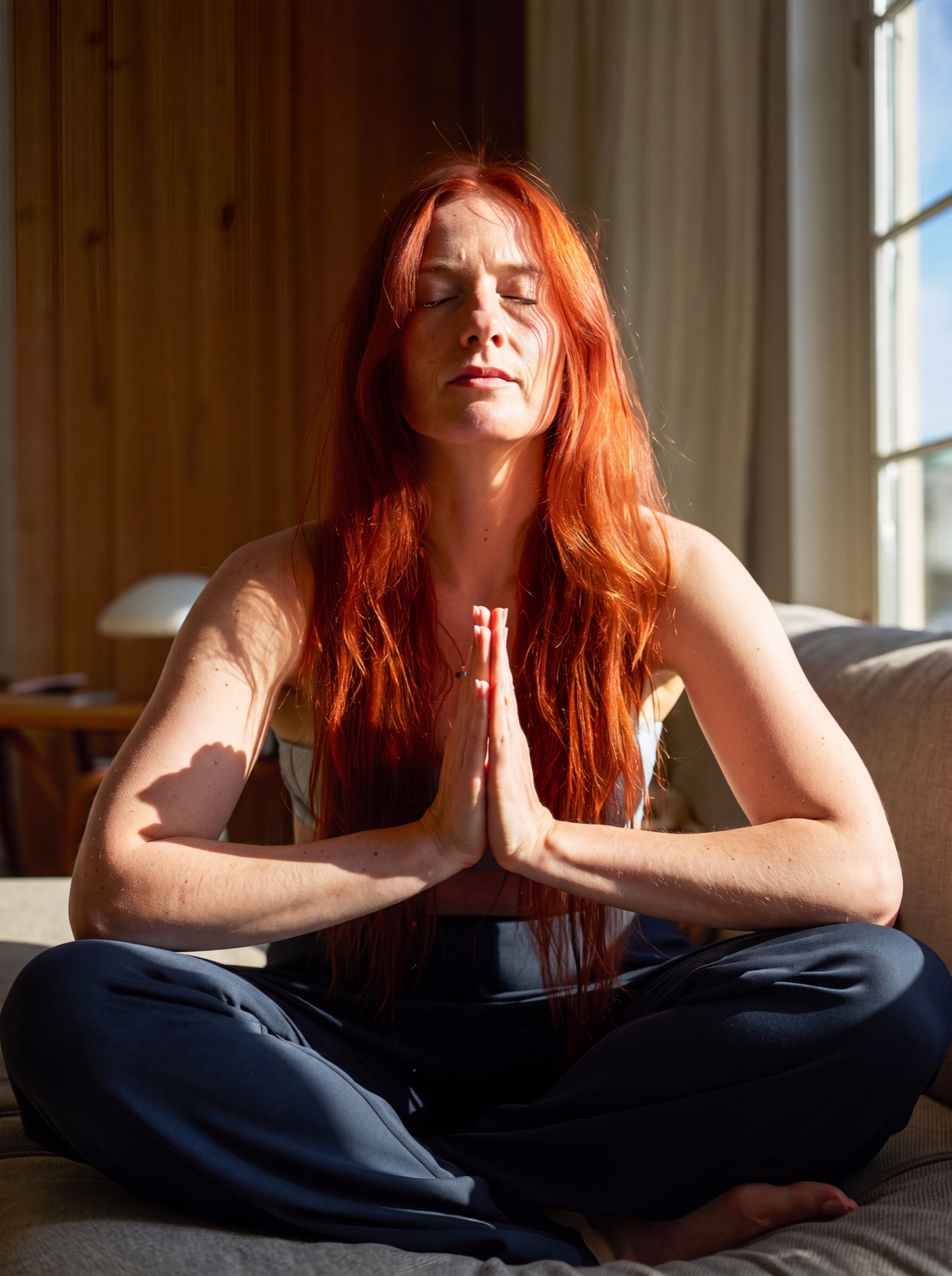 A woman sitting in stillness, eyes closed, hands together.