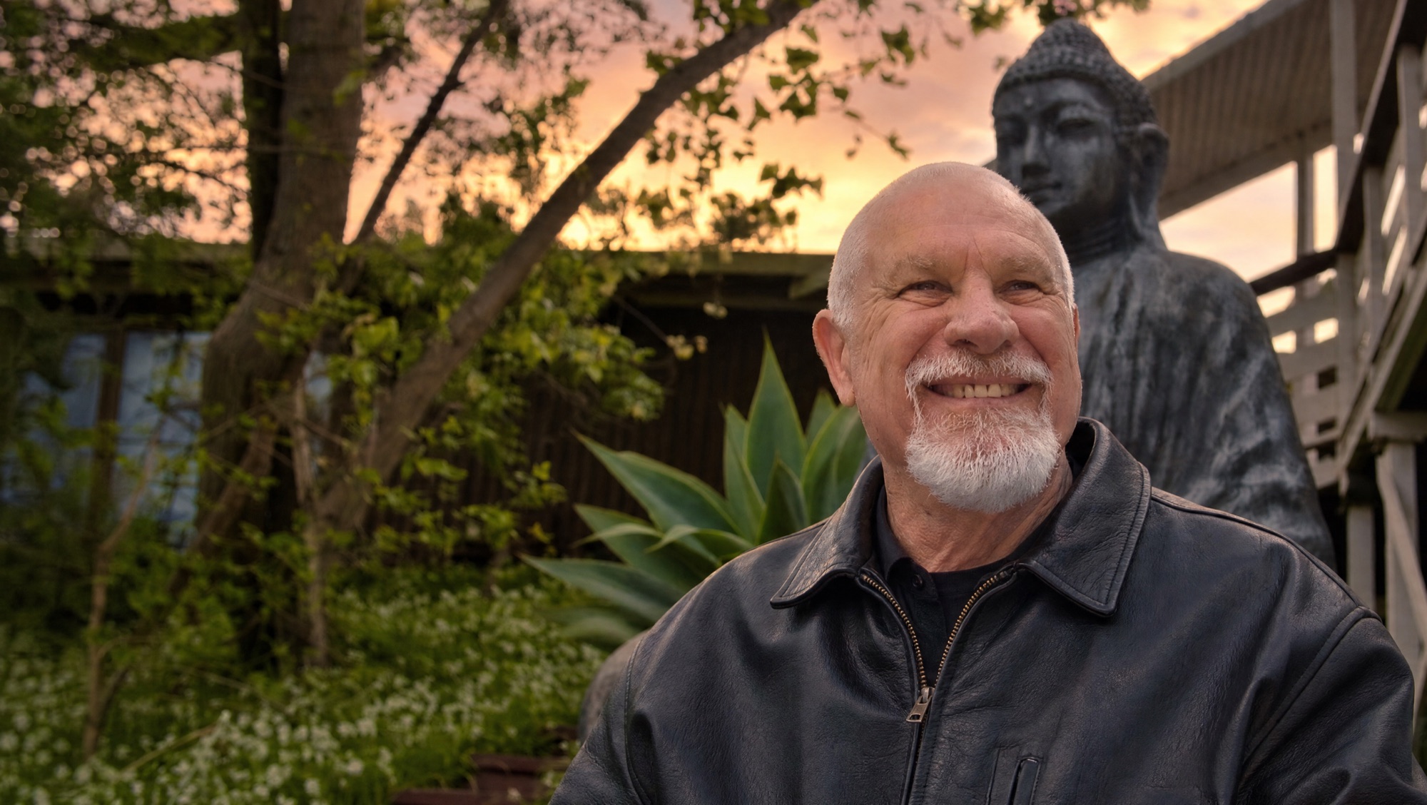 Vishrant smiling in a garden at dusk, a Buddha statue behind him